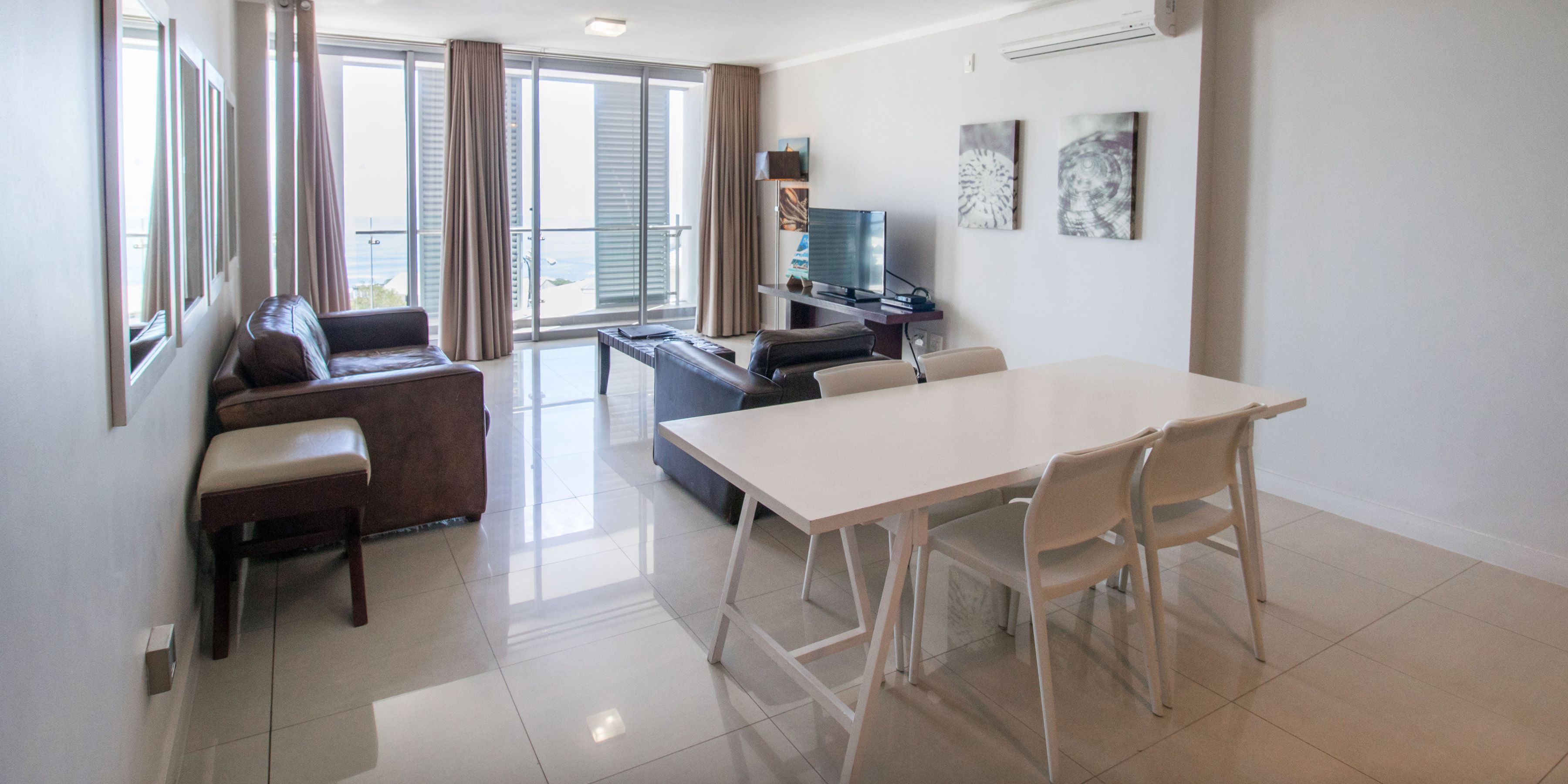 Una sala de estar moderna con un sofá, una mesa de comedor con sillas, un televisor y obras de arte en la pared.