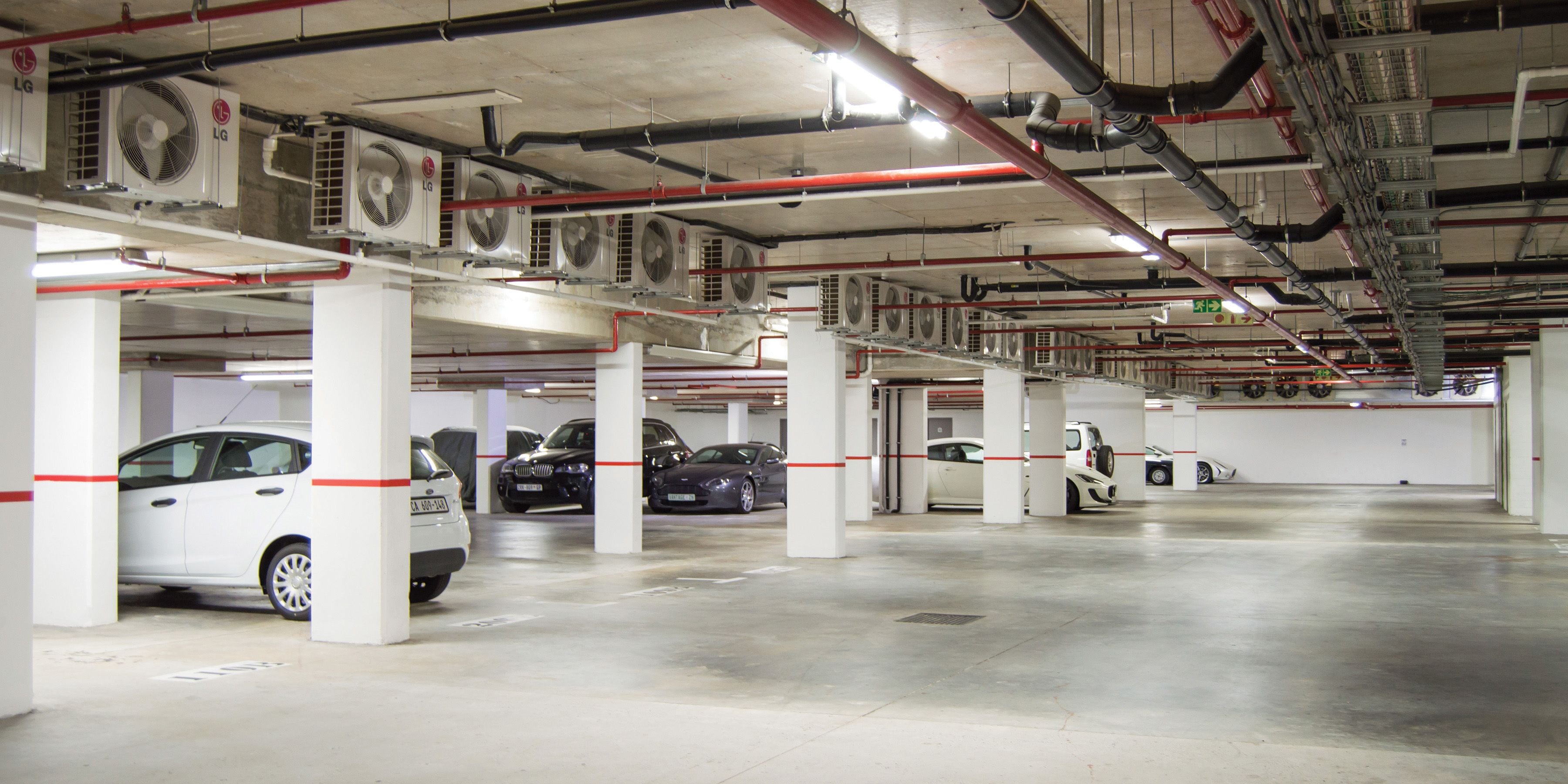 Useita kerroksia sisältävä pysäköintihalli, jonka valkoisten pylväiden alla on useita parkissa olevia autoja.