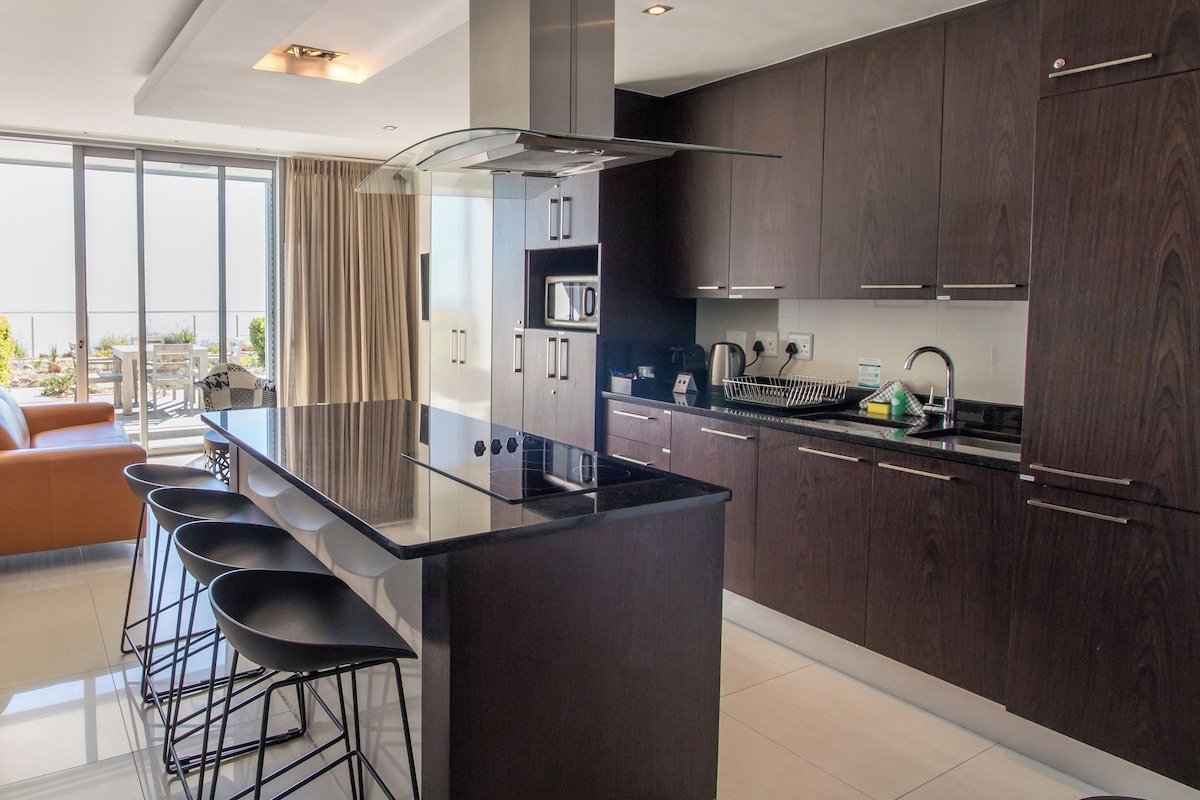 A modern kitchen with a central island, dark wooden cabinets, and a view to the outside.