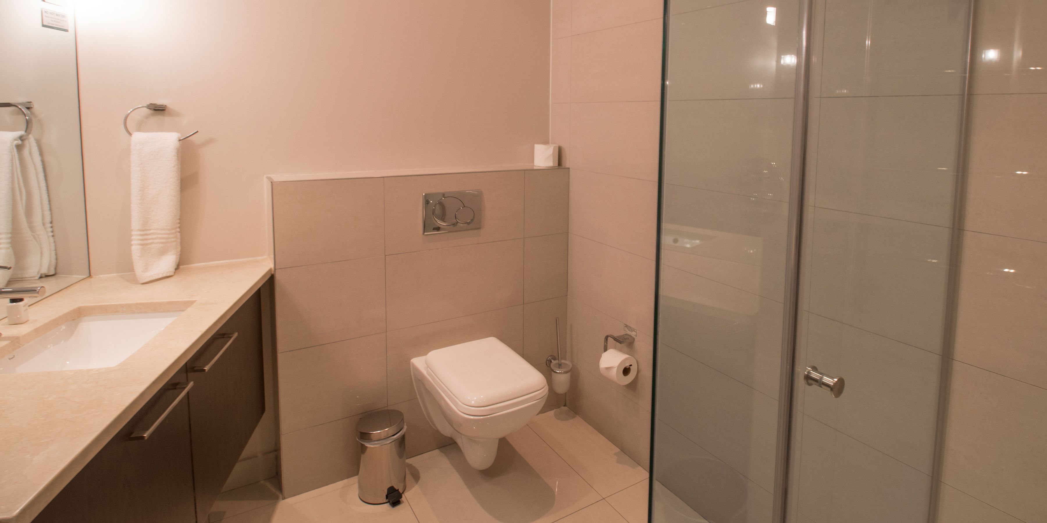 Et moderne badeværelse med toilet, håndvask og brusekabine i glas.