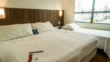 Une chambre d’hôtel avec un grand lit, un lit plus petit et une fenêtre donnant sur la ville.