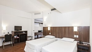A hotel room with two single beds, a desk with a TV, a chair, and a small kitchenette. - Firenze Business Hotel (Palhoça)