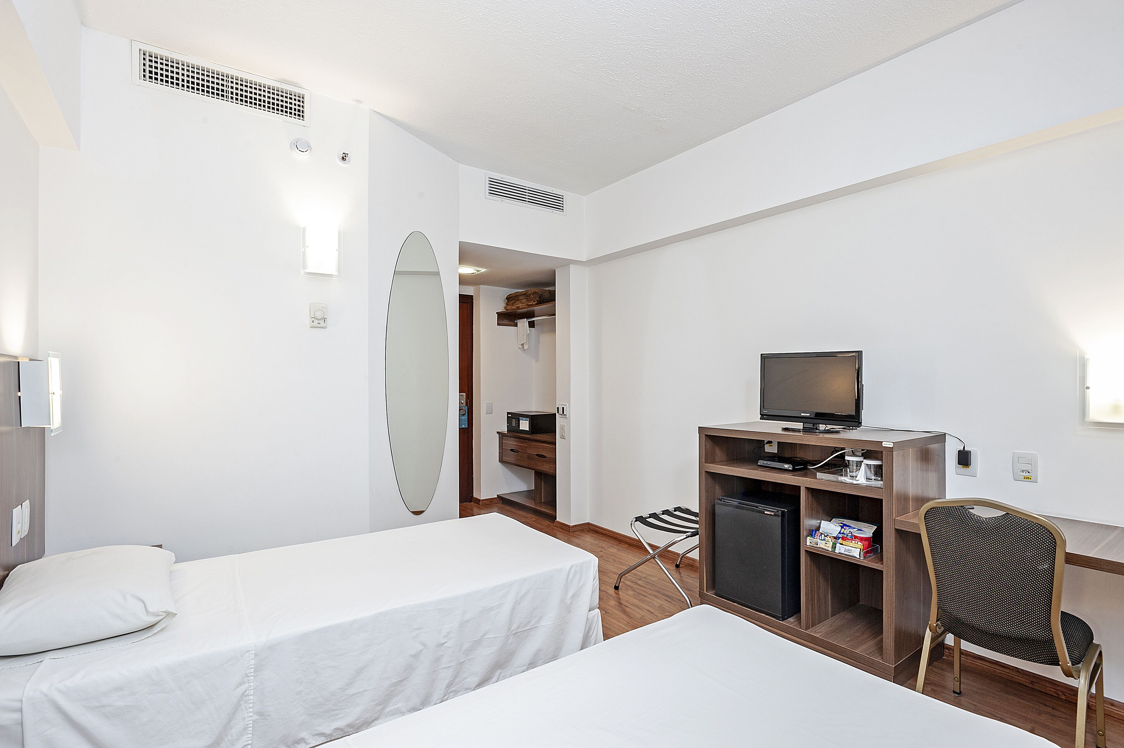 A hotel room with two single beds, a TV, a small fridge, and a wardrobe.