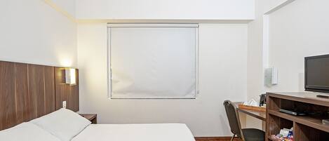 Habitación de hotel con cama, escritorio, silla, televisor y ventana con persianas.