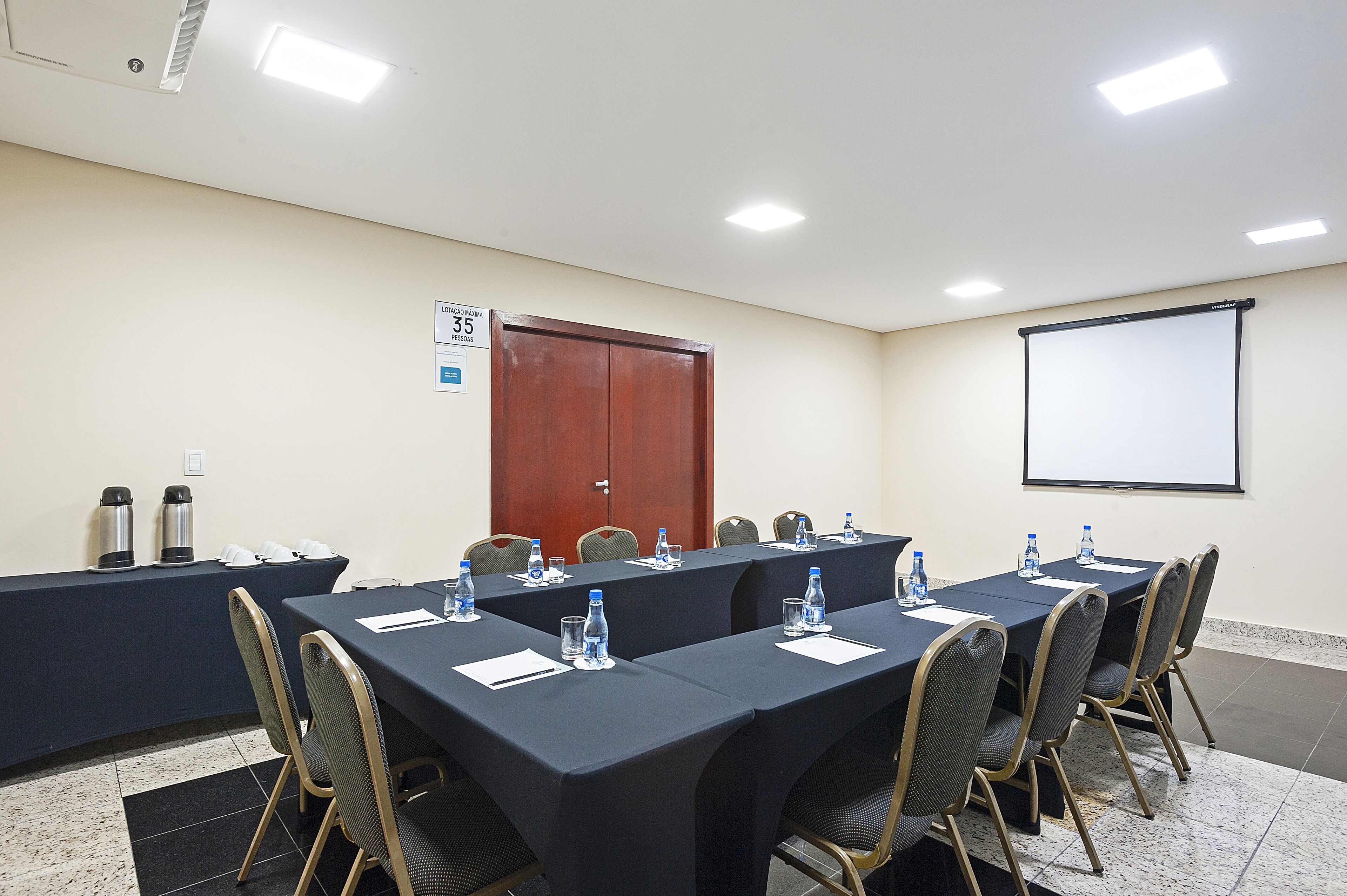 A conference room with a long table, chairs, a projector screen, and a door.