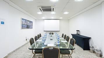 Un salón de conferencias con una mesa de vidrio, sillas, una pantalla de proyector y un mantel negro.