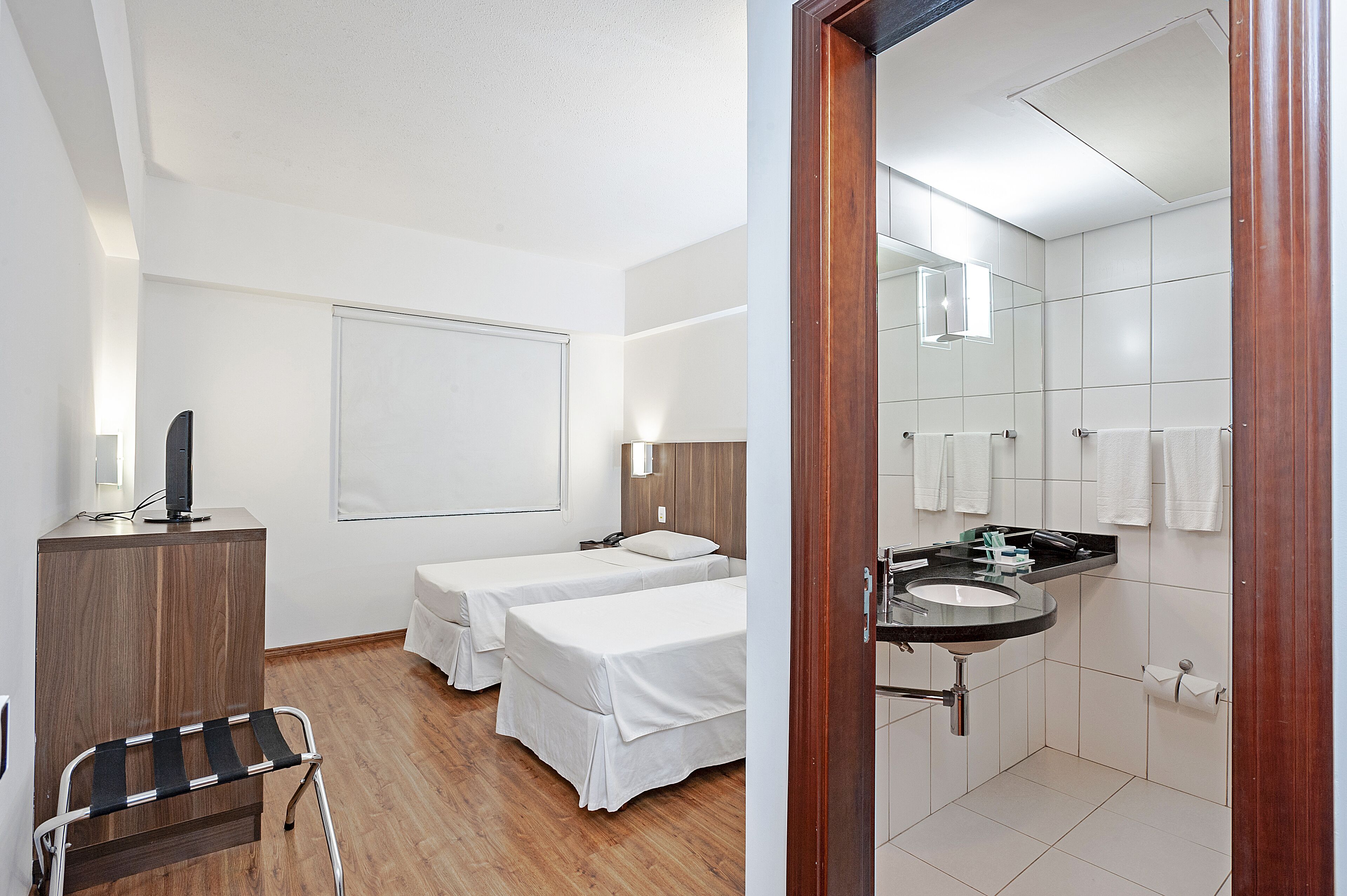 A hotel room with two beds, a desk with a computer, a chair, and a bathroom with a sink and mirror.