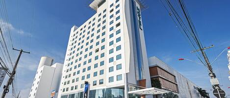A modern hotel with a prominent glass facade, multiple floors, and a rooftop antenna.