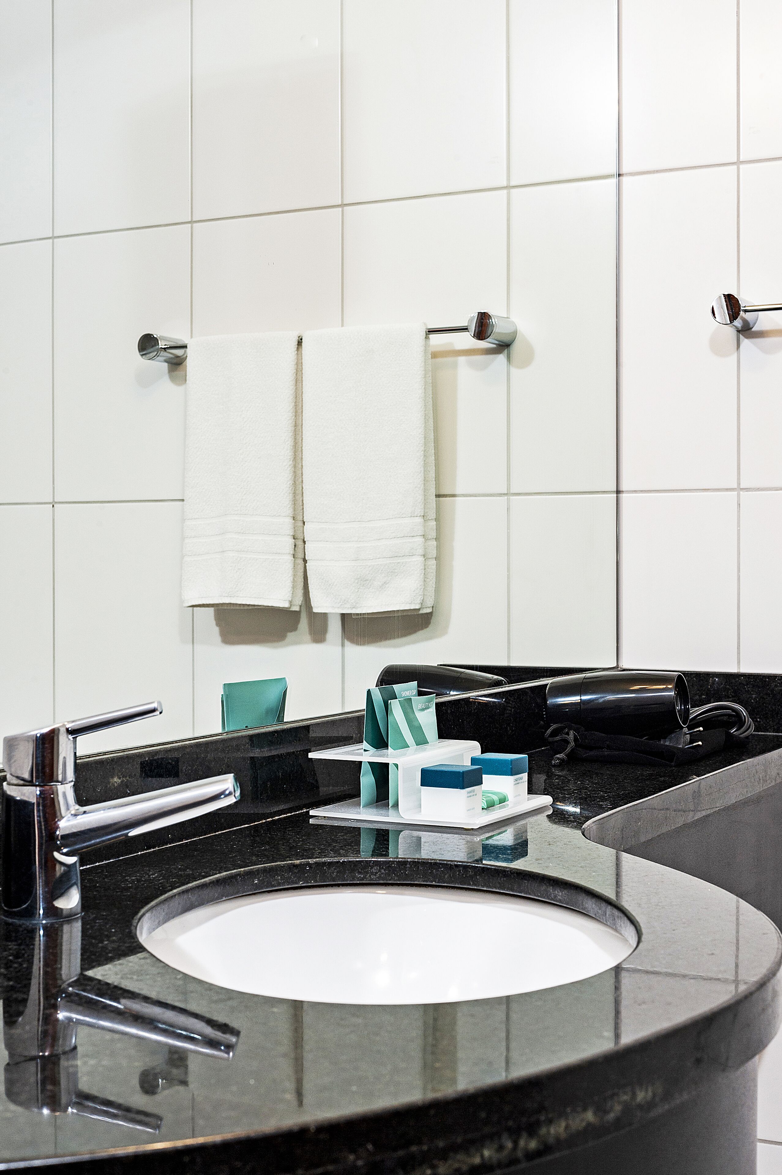 Un baño moderno con un lavamanos negro, grifos cromados y paredes cubiertas de azulejos blancos.