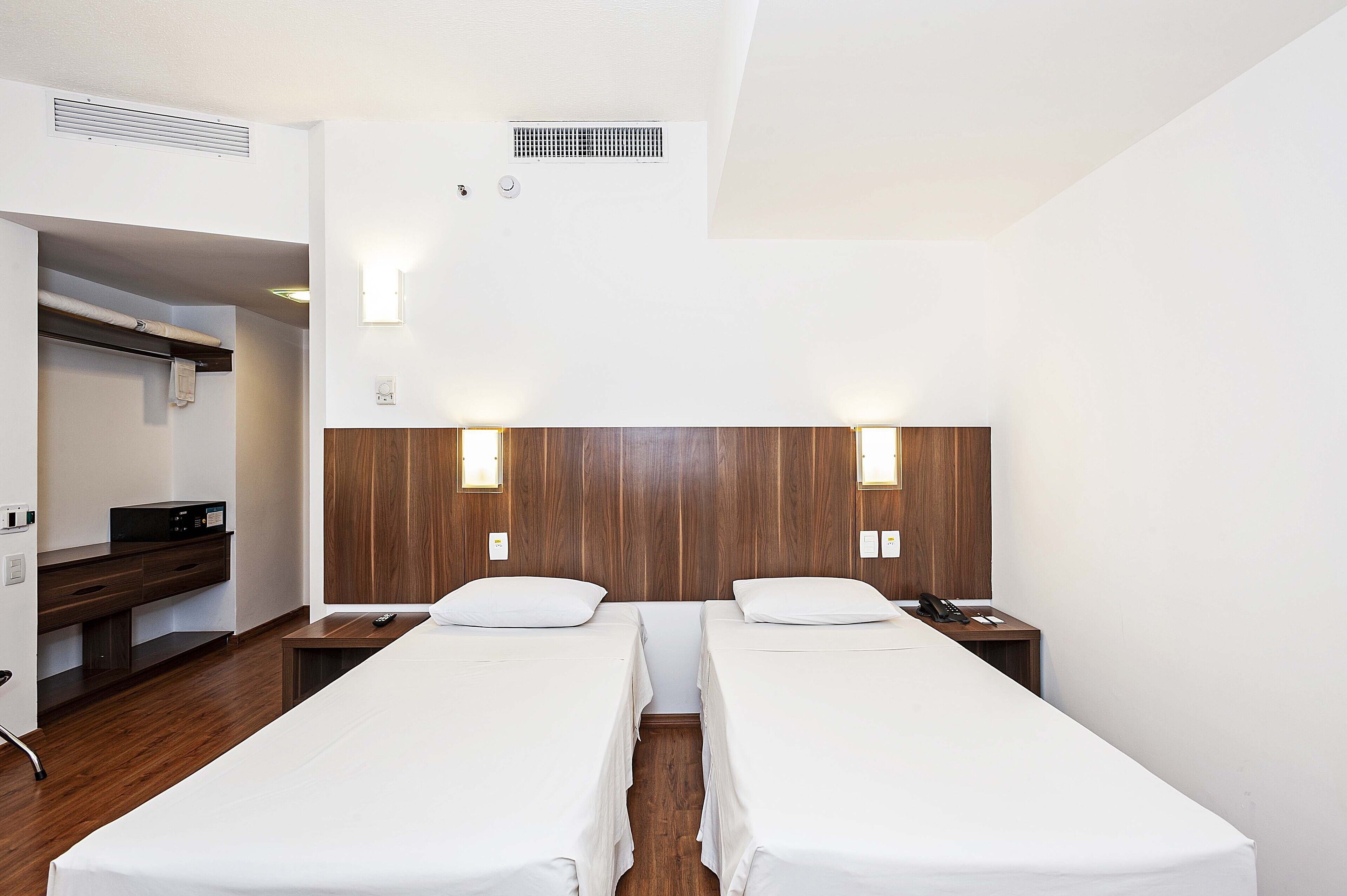 Une chambre d’hôtel avec deux lits simples, une tête de lit en bois, un bureau avec une chaise et une petite table avec un téléphone.