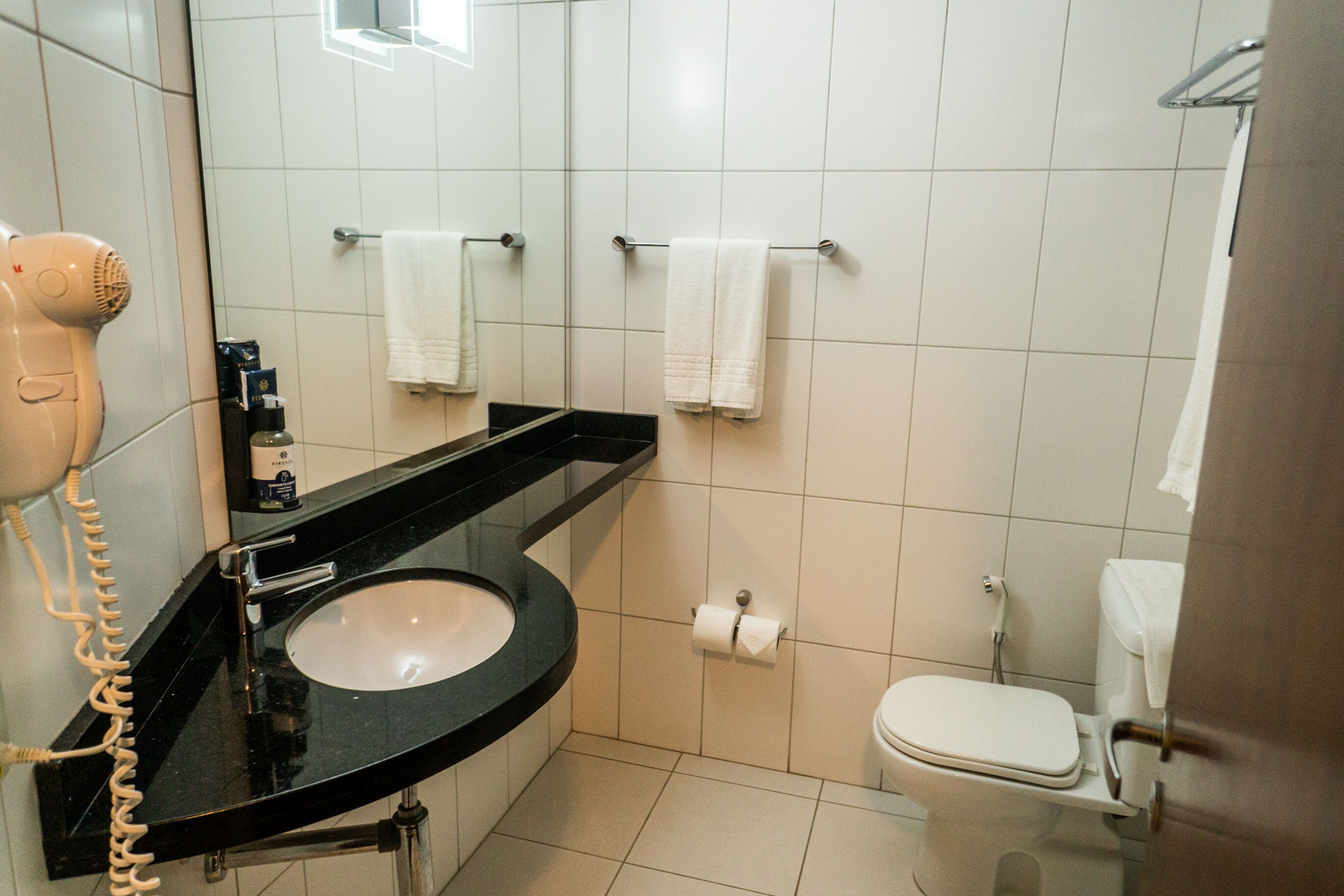 Un baño con lavamanos negro, inodoro blanco y un secador de pelo a la izquierda.