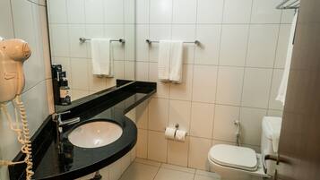Un baño con lavamanos negro, inodoro blanco y un secador de pelo a la izquierda.