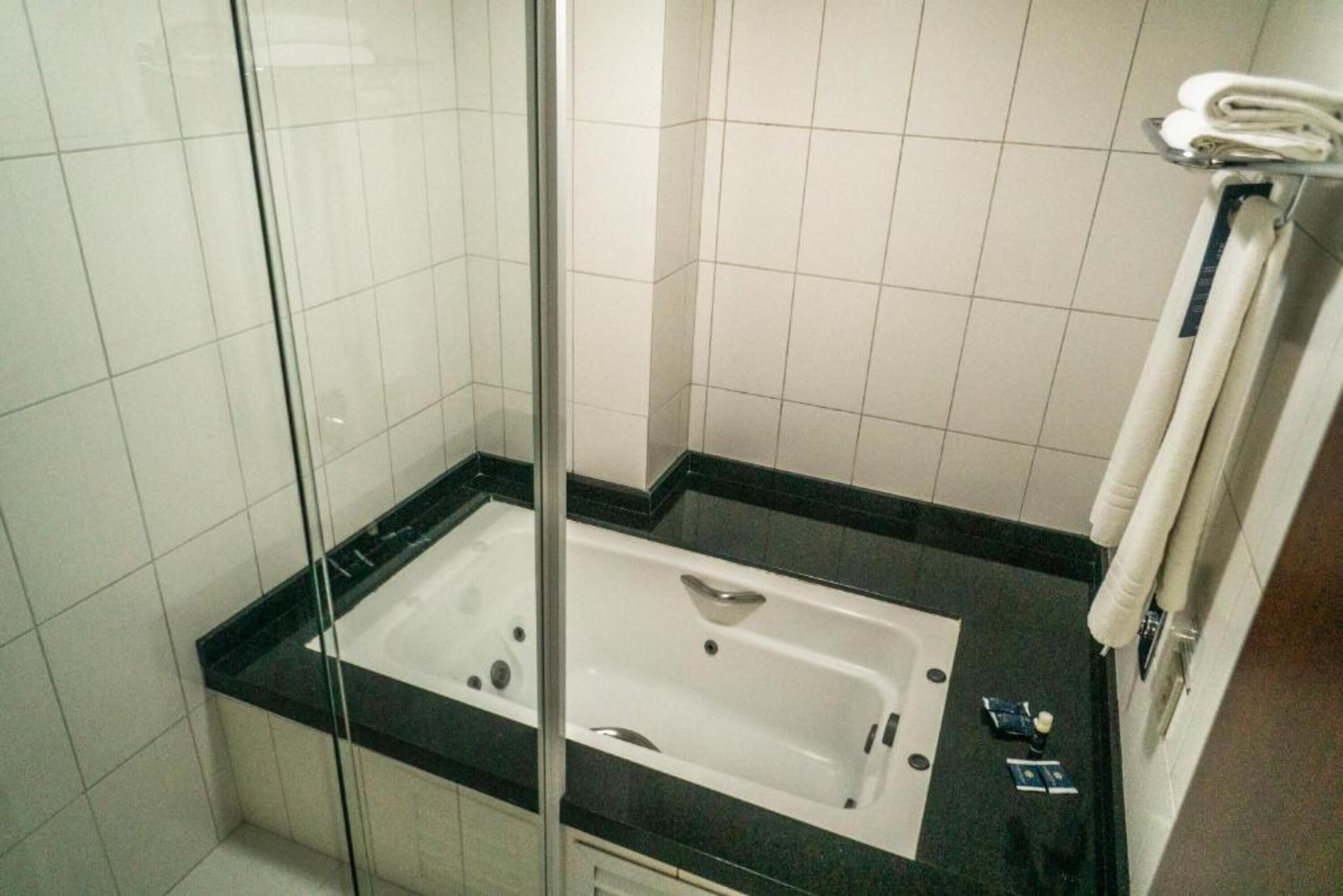A modern bathroom with a glass-enclosed shower, a white bathtub, and a black countertop.