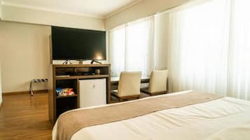 A hotel room with a bed, a desk with a chair, a television, and a small refrigerator.