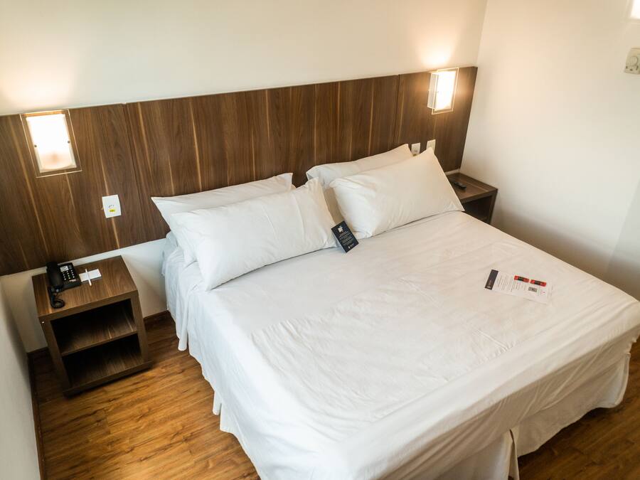 A hotel room with a wooden headboard, two bedside tables, a white bed with pillows, and a nightstand with a phone.