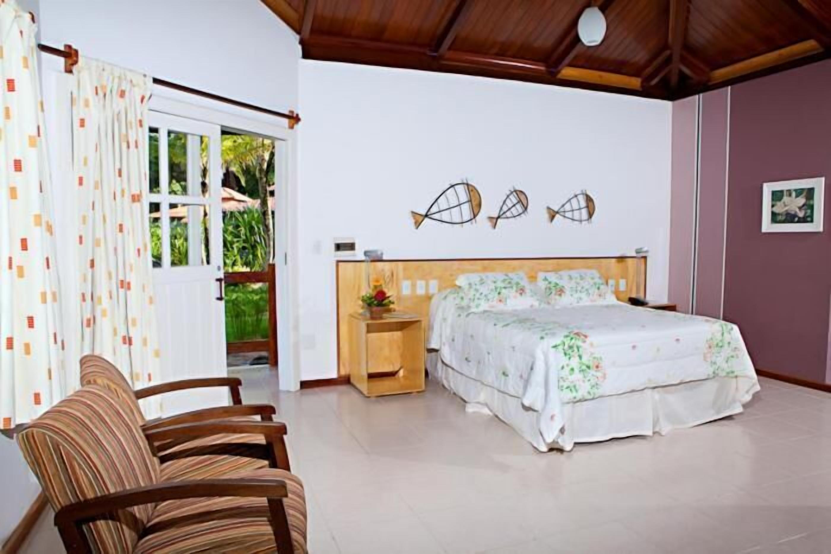 A bedroom with a bed, a chair, a nightstand, and a window with curtains.