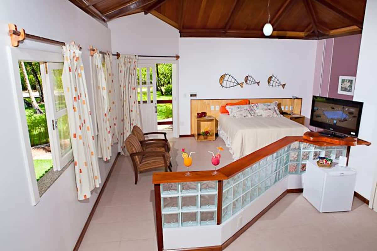 A bedroom with a bed, a TV, a desk, and a balcony with curtains.