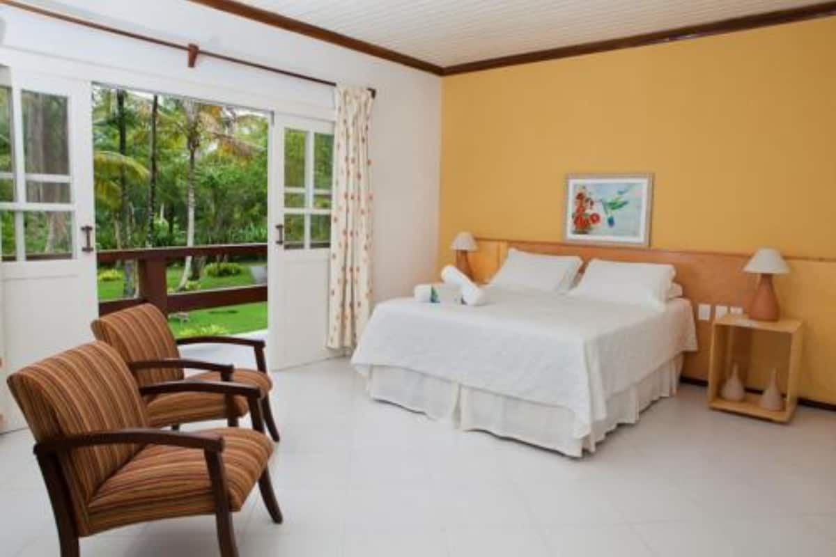 A bedroom with a bed, two bedside tables, a chair, and a window with a view of greenery.
