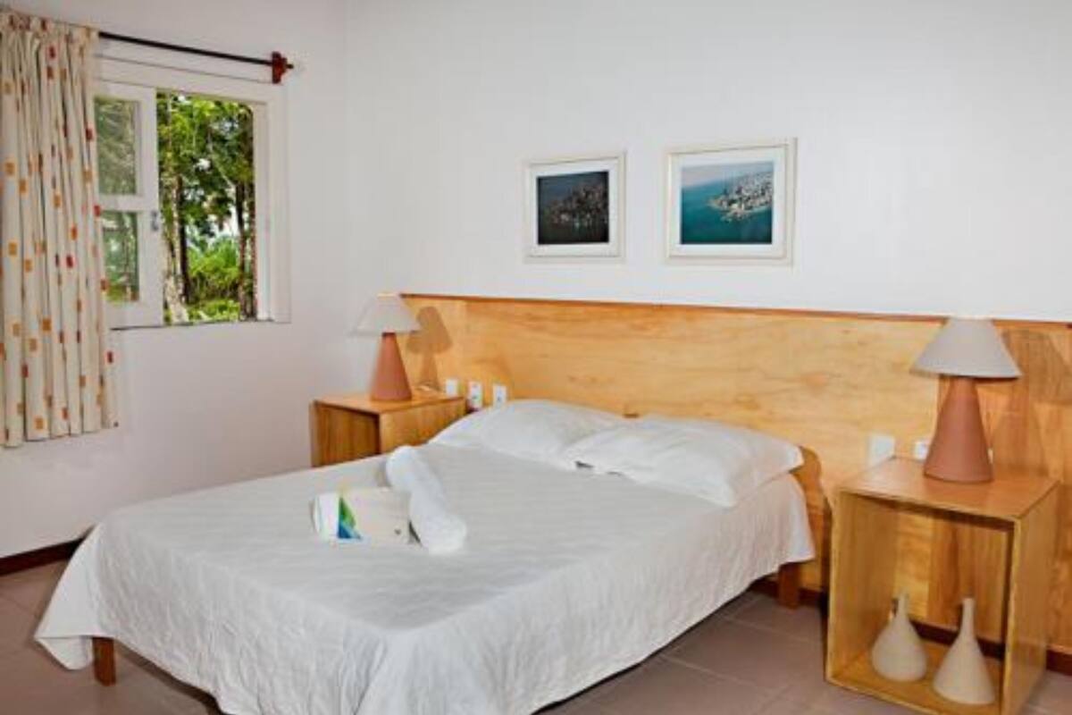 A neatly made bed with white linens, a wooden headboard, two bedside tables with lamps, and two framed pictures on the wall.