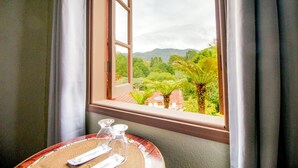 Ein Zimmer mit Fenster und Blick auf eine üppige Landschaft, ein Tisch mit Unterlage und zwei Glasflaschen.