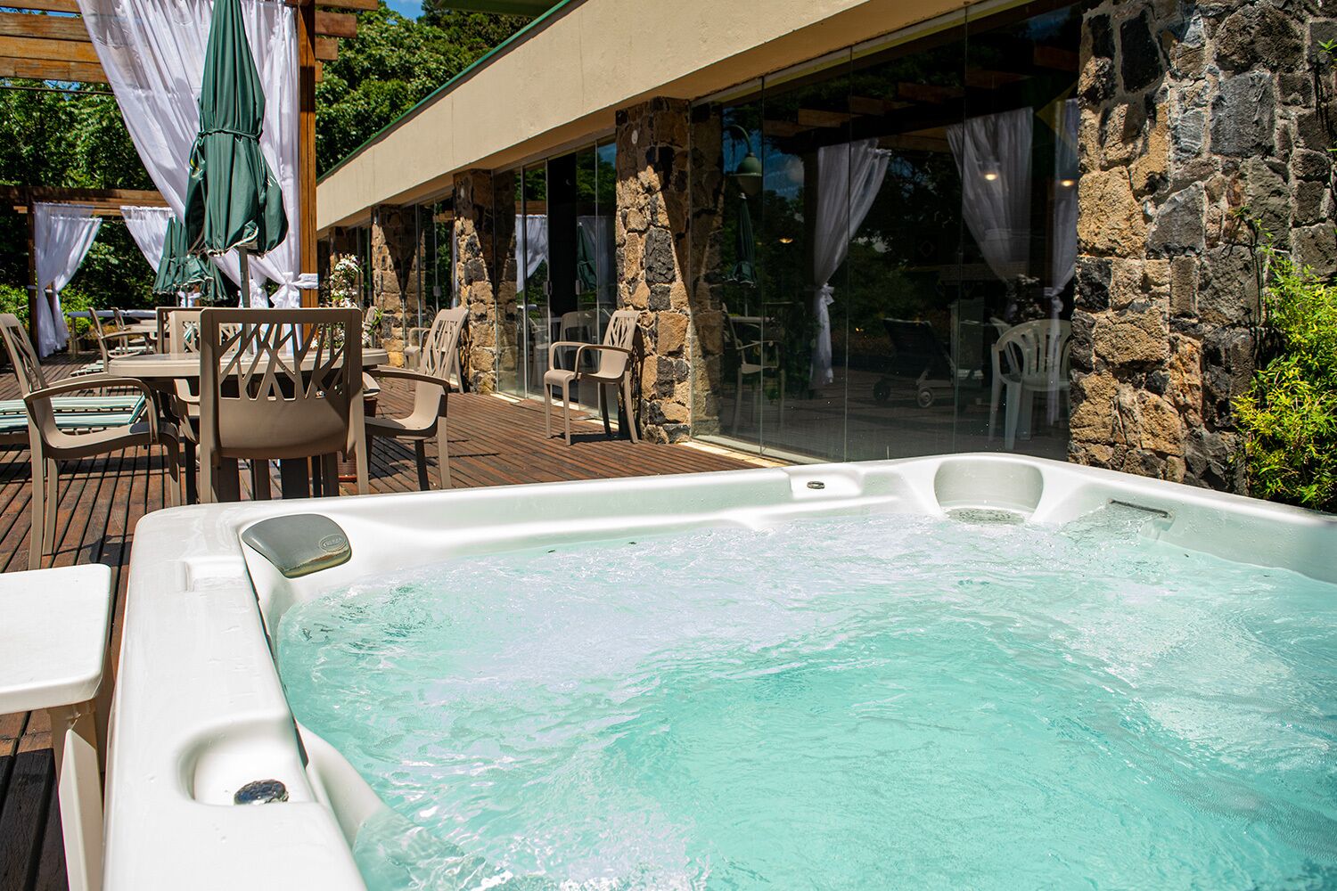 A hot tub with clear water, surrounded by stone walls and wooden deck chairs.