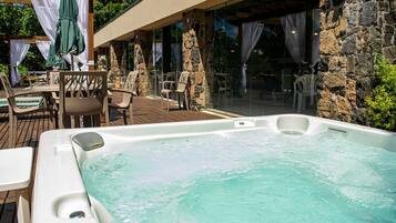 A hot tub with clear water, surrounded by stone walls and wooden deck chairs.