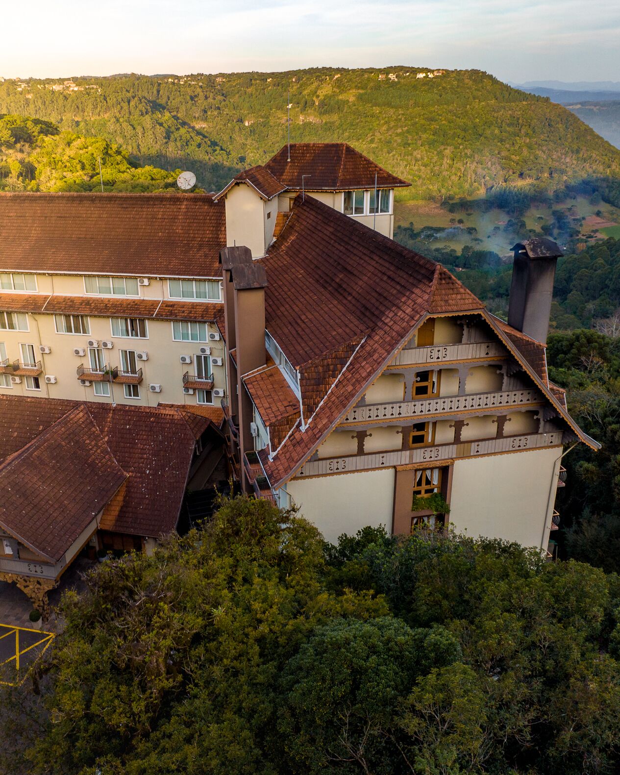 A multi-story building with a sloped roof, surrounded by dense greenery and hills in the background.