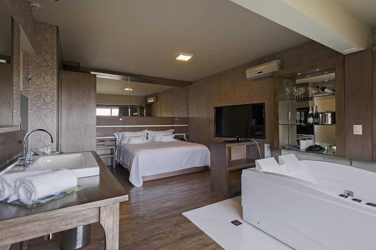 A modern hotel room with a large bed, a separate bathroom with a bathtub, a TV, and a minibar.