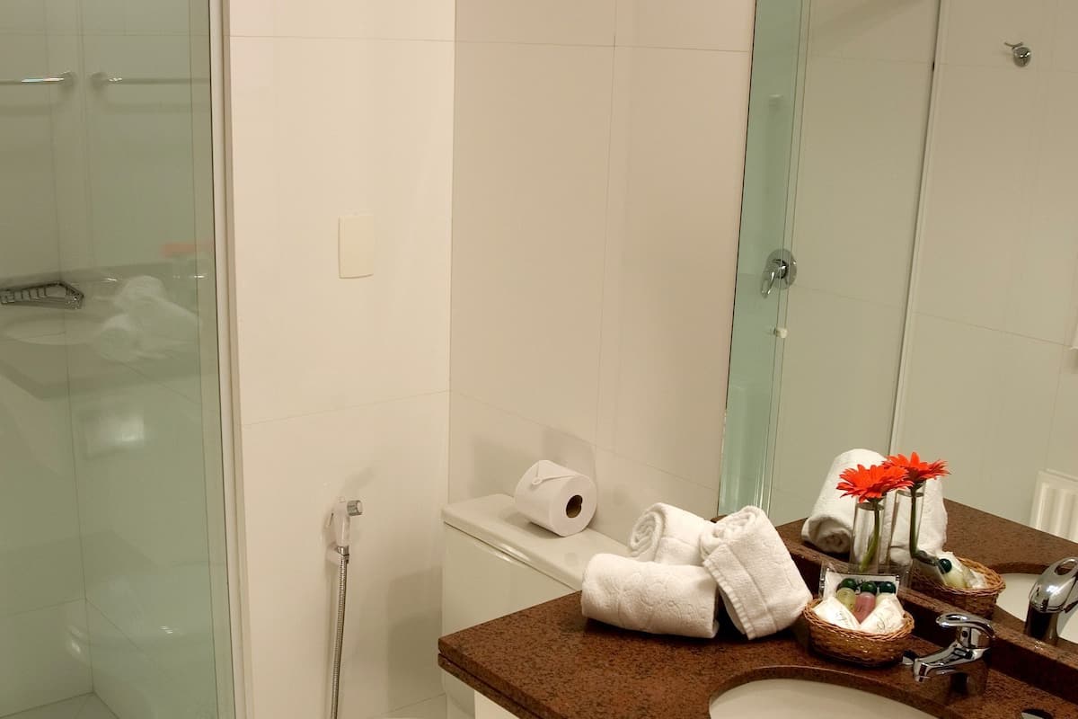 A bathroom with a glass shower enclosure, a toilet, a sink with a mirror, and a trash can.