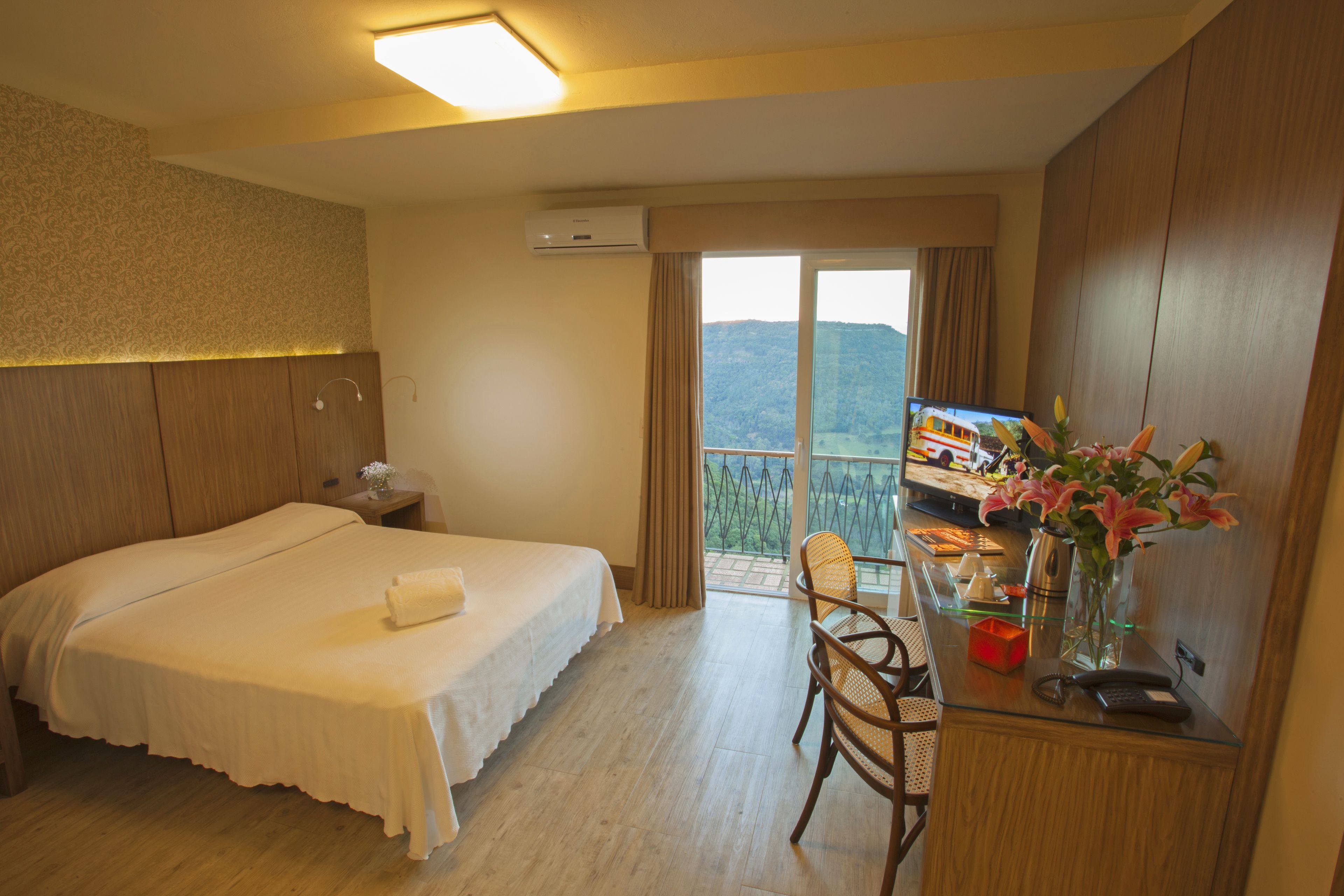 Quarto de hotel com cama, escrivaninha com computador, cadeira e janela com vista para uma montanha.