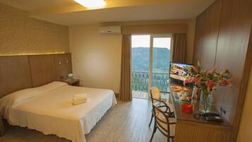 Quarto de hotel com cama, escrivaninha com computador, cadeira e janela com vista para uma montanha.