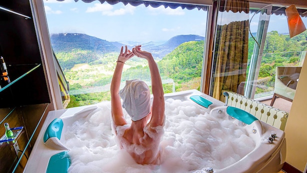 A person in a bathtub with a scenic view of mountains and greenery. - Villa Bella Hotel & SPA Gramado (Gramado)