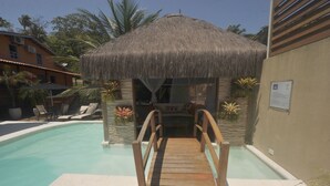 A wooden deck leading to a pool area with a thatched-roof structure. - Pousada Mareia (Cairu)