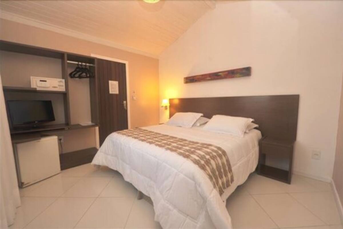 A bedroom with a bed, a desk with a computer, and a TV.