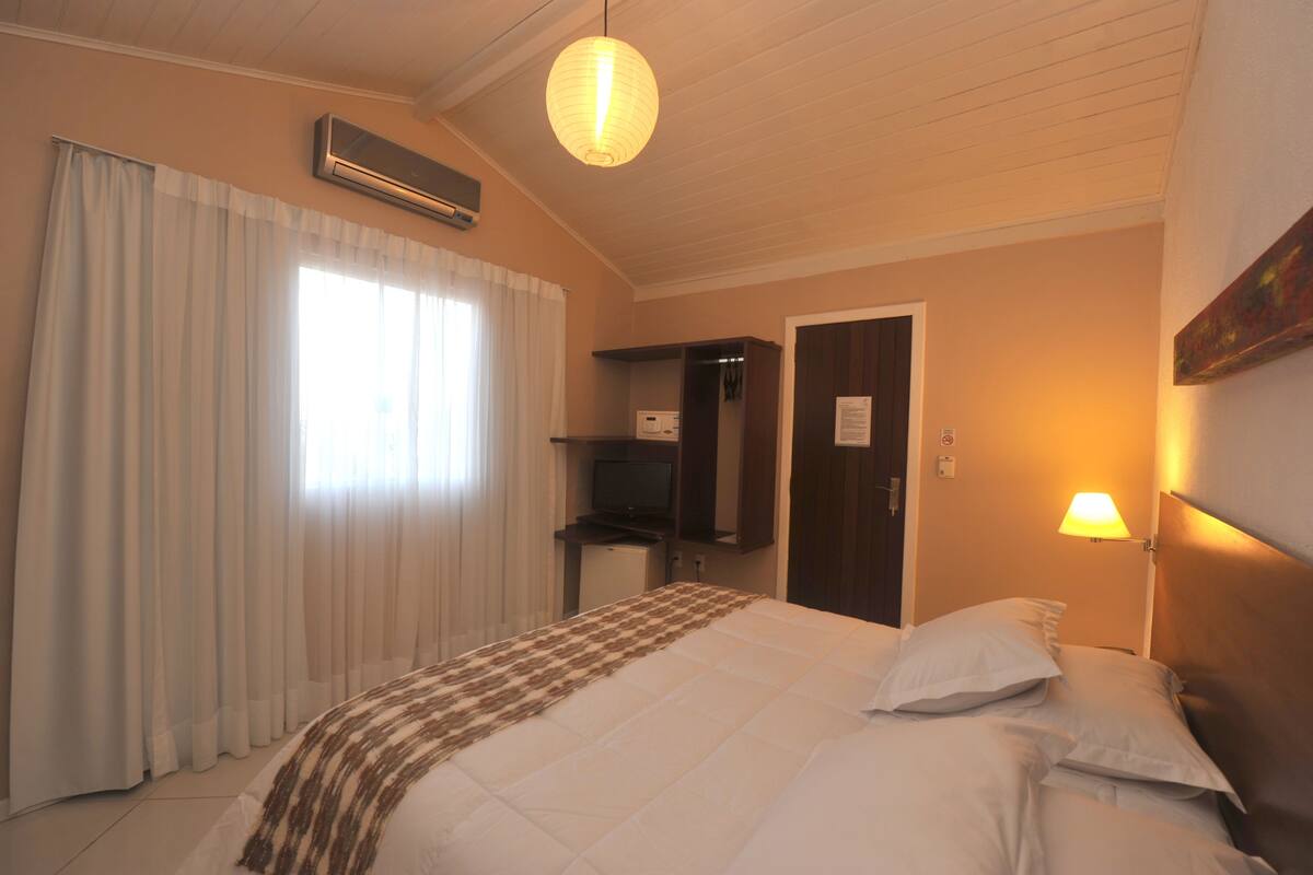 A hotel room with a bed, curtains, a desk, a television, and a lamp.