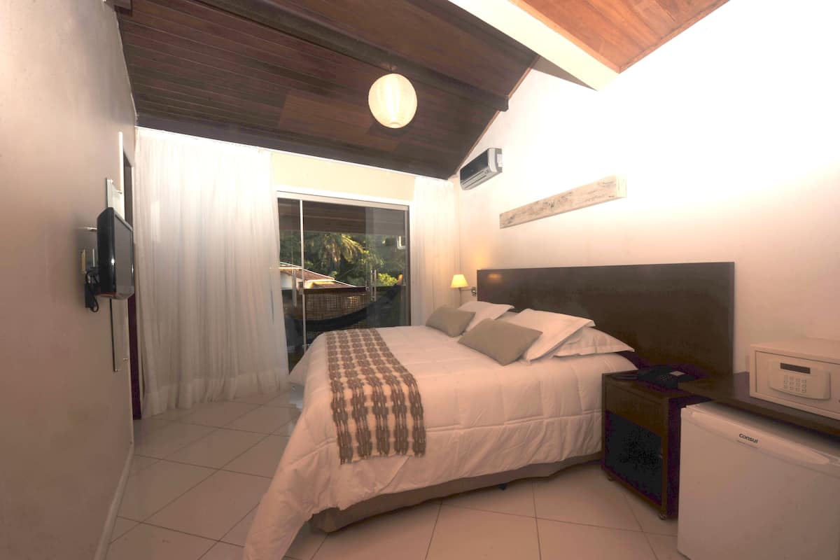 A bedroom with a bed, bedside table, lamp, and a small refrigerator.