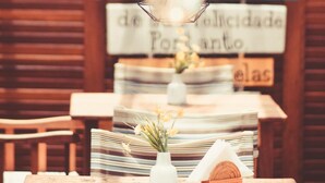A wooden table with a hanging light fixture, a small white vase with flowers, and a stack of magazines. - Pousada Mareia (Cairu)
