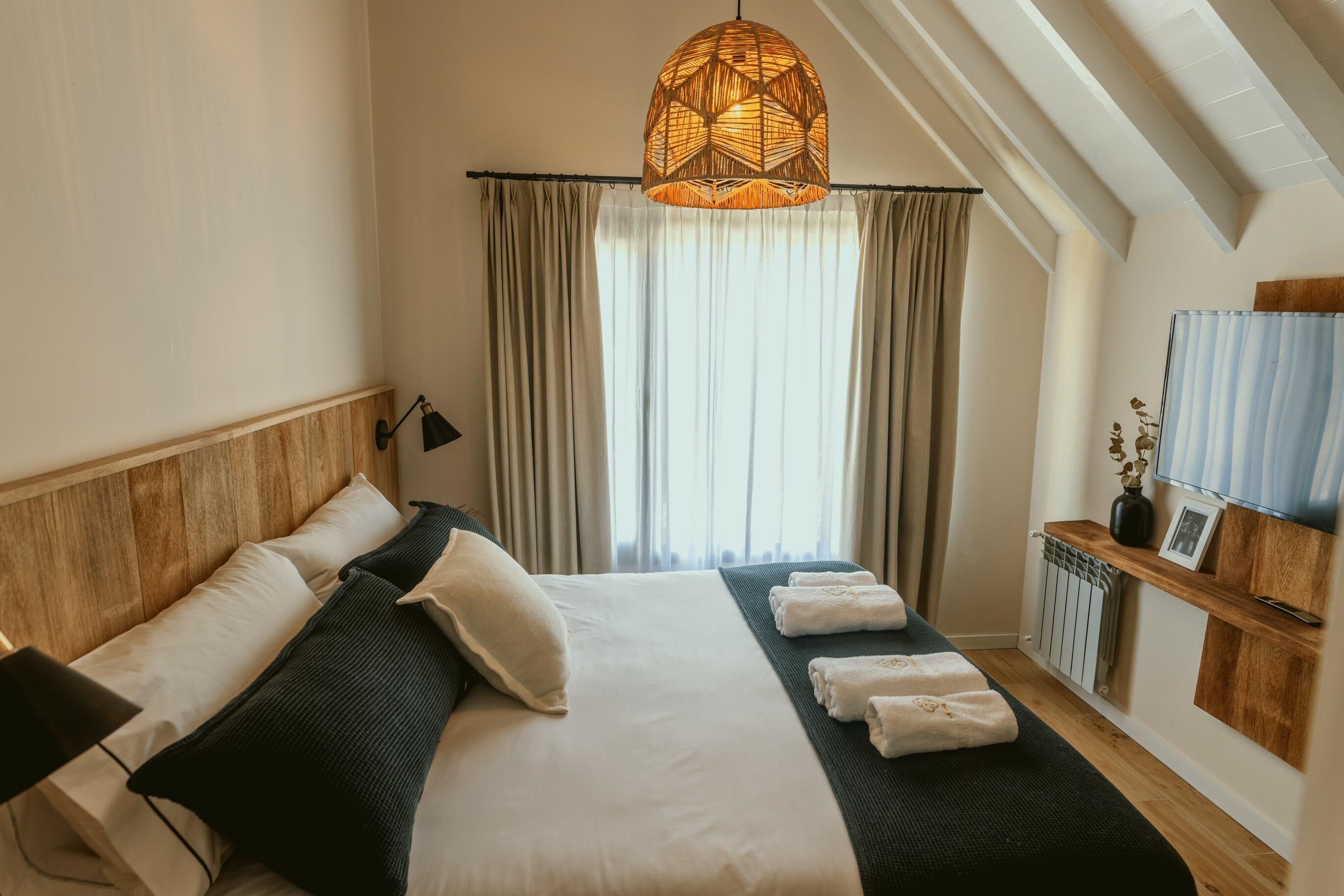 A bedroom with a large bed, a hanging light fixture, a radiator, and a shelf with a picture frame.