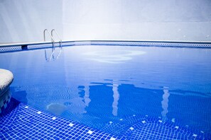 Una piscina interior con agua azul cristalina, bordes de azulejos y escaleras de metal.