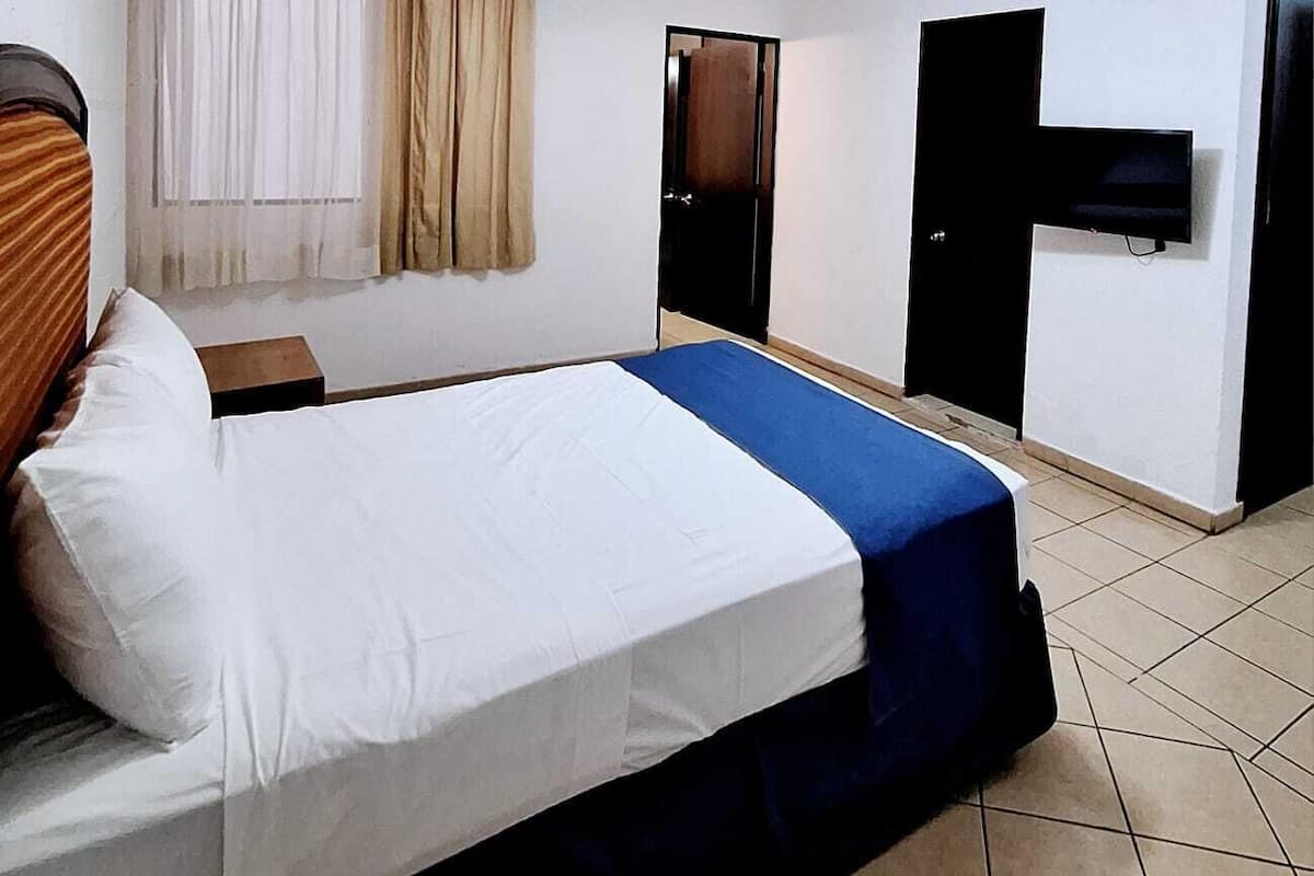 A hotel room with a bed, a TV, and a ceiling fan.