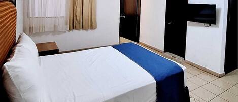 A hotel room with a bed, a TV, and a ceiling fan.