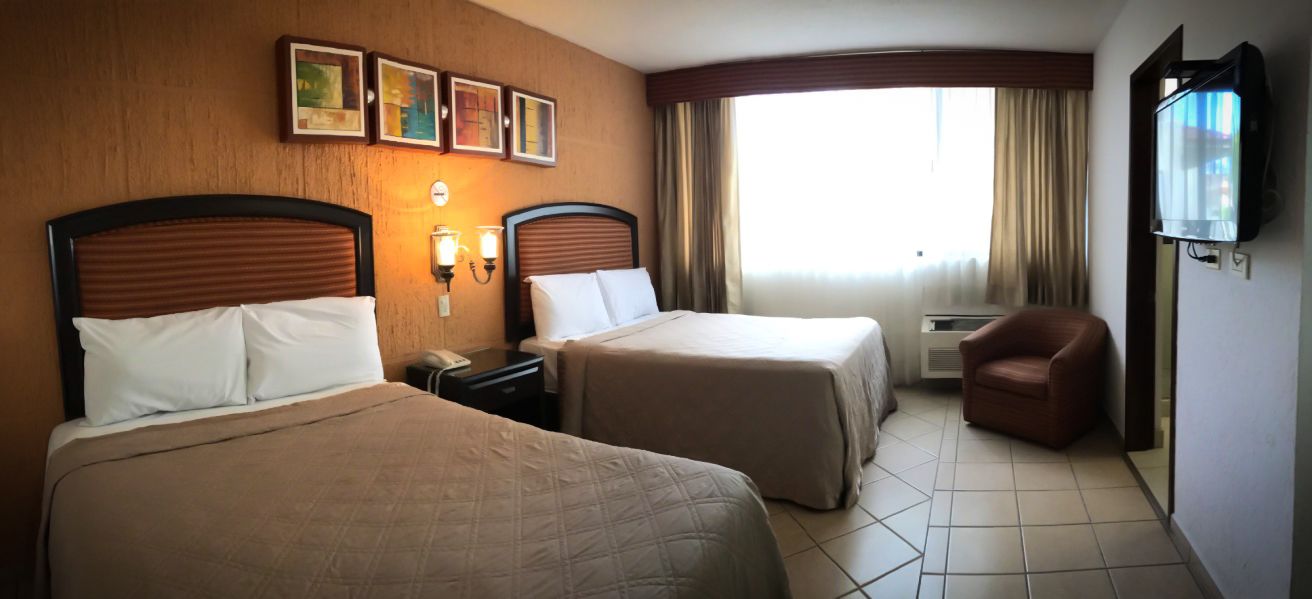 A hotel room with two beds, a TV, a chair, and a window with curtains.