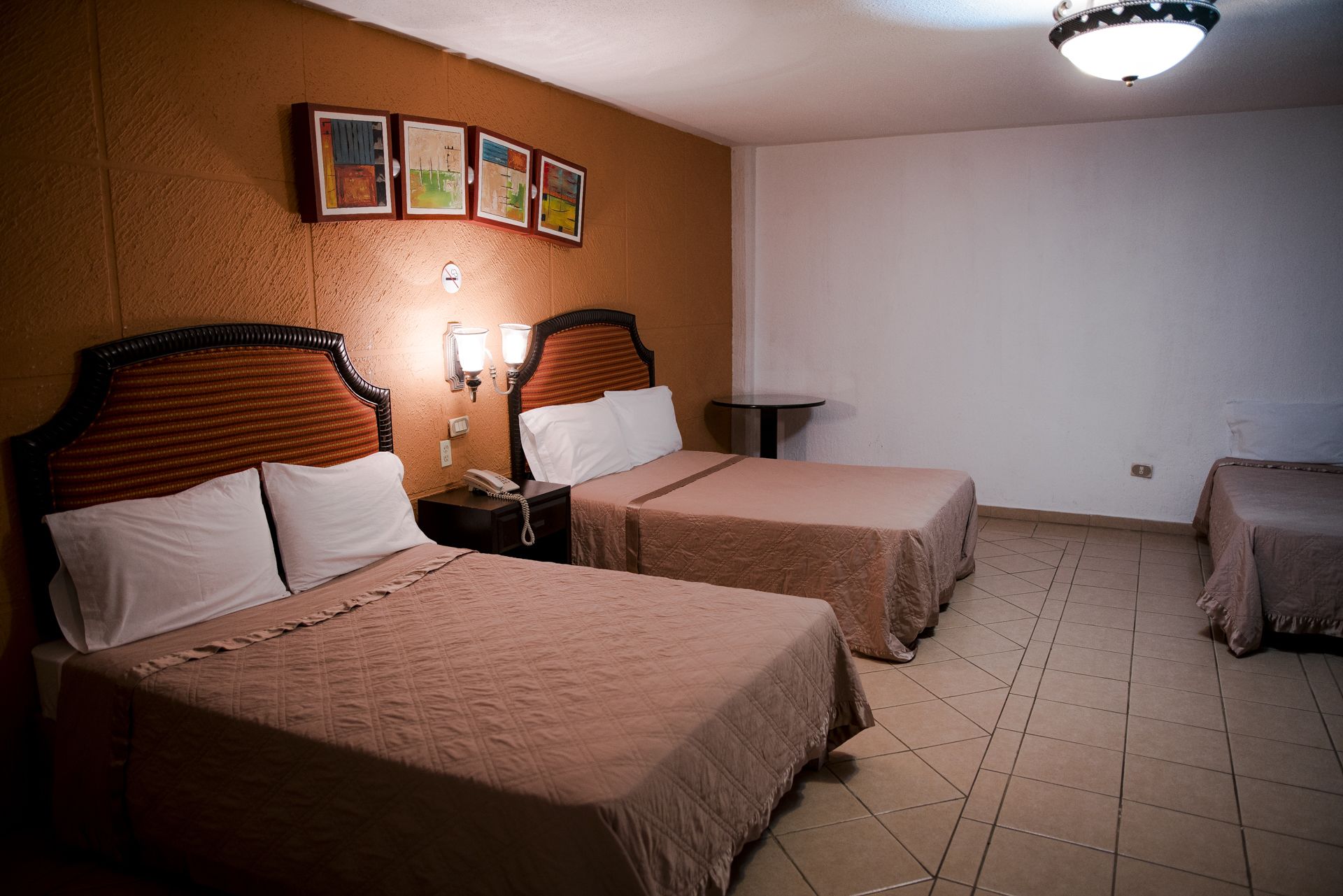 Habitación de hotel con dos camas, una mesita pequeña y un reloj en la pared.