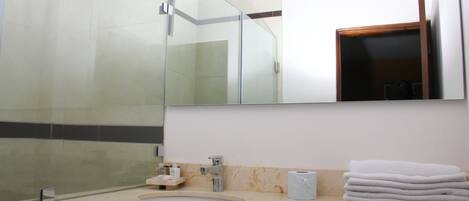 Un baño con cabina de ducha de vidrio, un lavabo con encimera de mármol y un espejo sobre el lavabo.