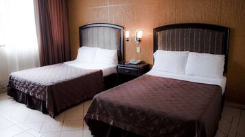 A hotel room with two beds, each with a headboard and a nightstand with a phone.