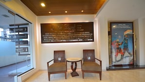 A reception area with a wall-mounted sign detailing hotel services and a poster of mountaineers. Two wooden chairs and a small table are in the foreground. - The Legend Inn Nagpur (Nagpur)