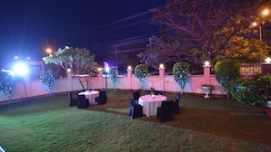 An outdoor patio area with tables and chairs, surrounded by trees and decorative lights. - The Legend Inn Nagpur (Nagpur)