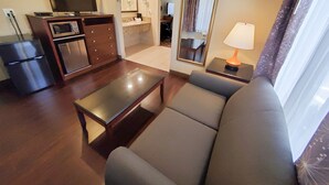 Una sala moderna con un sofá, una mesa de centro, un televisor, un microondas, un refrigerador pequeño y un comedor con una mesa y sillas.