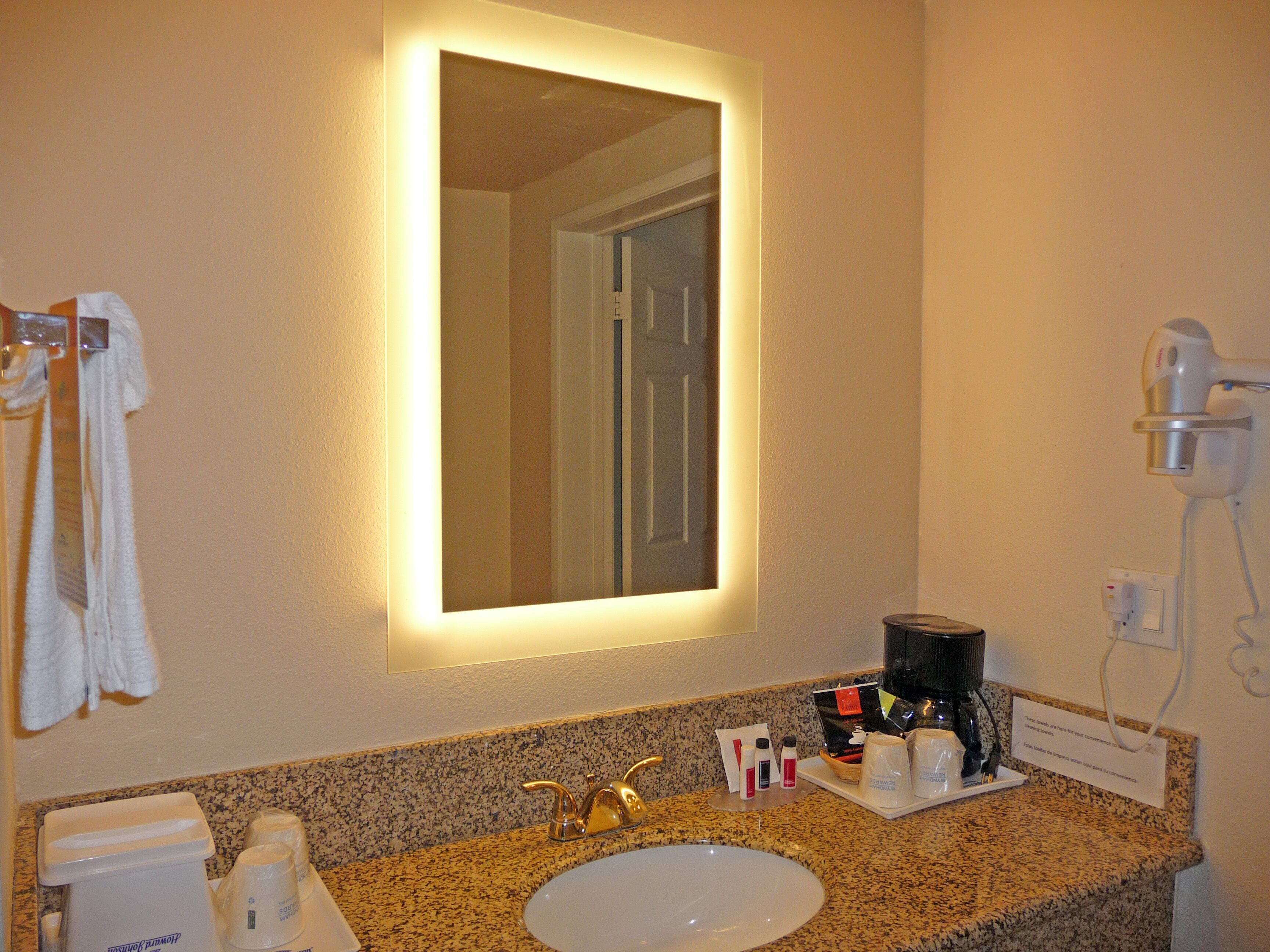 A hotel bathroom with a sink, mirror, towel rack, and a hairdryer.