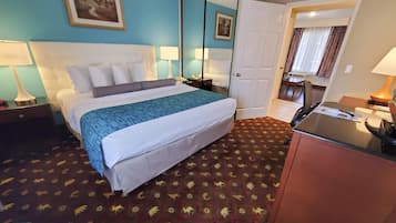 A hotel room with a bed, bedside lamps, a desk, a mirror, and a door leading to another room.